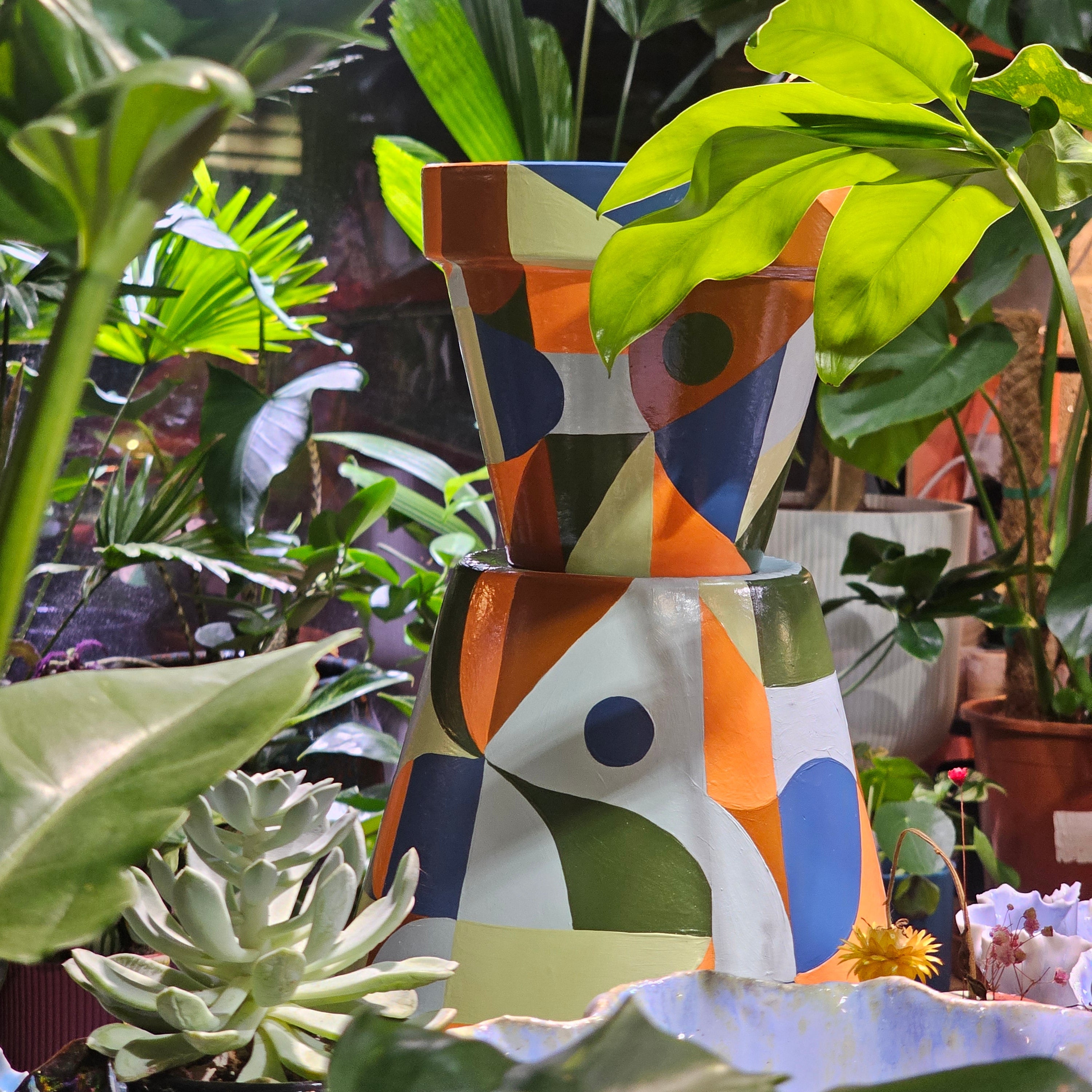 Colorful abstract art piece with geometric patterns surrounded by green plants